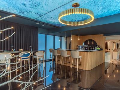 Moderner Hotelbarbereich mit hohen Stühlen, blauer Decke und elegantem Holzinterieur.