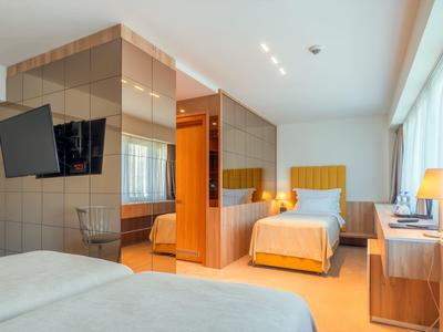 Helles Hotelzimmer mit zwei Einzelbetten, großem Fenster, Fernseher und modernem Holzinterieur.