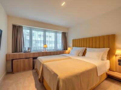 Modernes Schlafzimmer mit Doppelbett, braunen Vorhängen, Holzsideboard und Wandfernseher.