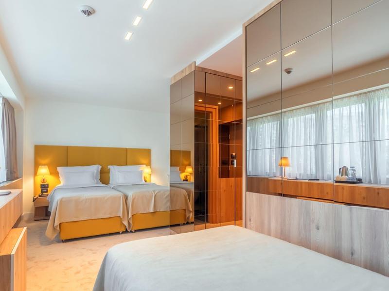 Helles, modernes Schlafzimmer mit großen Fenstern, zwei Einzelbetten und großem Spiegel an der Wand.