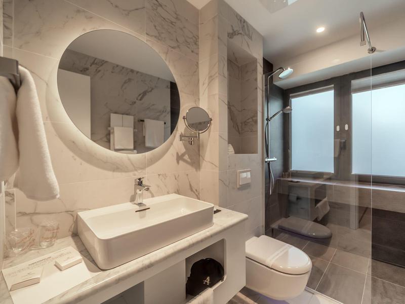 Modernes Badezimmer mit rundem Spiegel, weißem Waschbecken, WC und großem Fenster mit Milchglas.