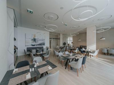 Modernes Restaurant mit hellen Holzböden, grauen Stühlen und runden weißen Deckenleuchten.