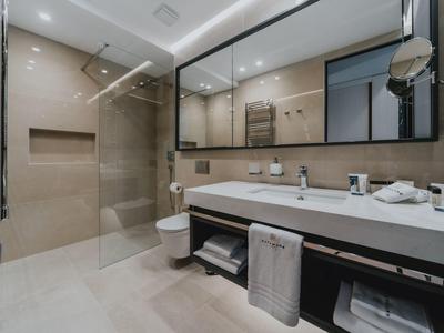 Moderne Bad mit Glasdusche, großem Spiegel, Doppelwaschbecken und hellen Fliesen.