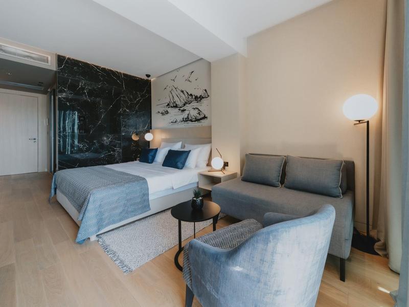 Modern eingerichtetes Hotelzimmer mit grauem Sofa, Doppelbett und schwarzer Marmorwand.