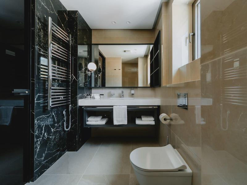 Modernes Badezimmer mit schwarzer Marmorwand, großem Spiegel und weißer Toilette nahe hellem Fenster.