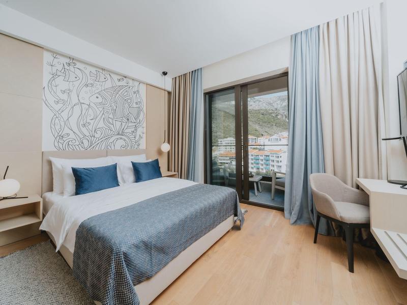 Modernes Schlafzimmer mit großem Bett, grauen und blauen Bettwaren, Fenster mit Blick auf Berglandschaft.