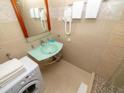 Kleines Badezimmer mit Glaswaschbecken, Waschmaschine, Handtüchern und Duschbereich mit Steinmosaikboden.