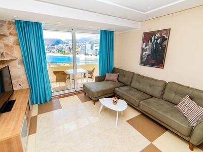 Helles Wohnzimmer mit brauem Ecksofa, blauem Vorhang, Fernseher und kleinem weißen Tisch.