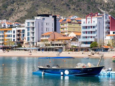 Booten op rustig water voor een strandpromenade met kleurrijke gebouwen en bergen op de achtergrond.