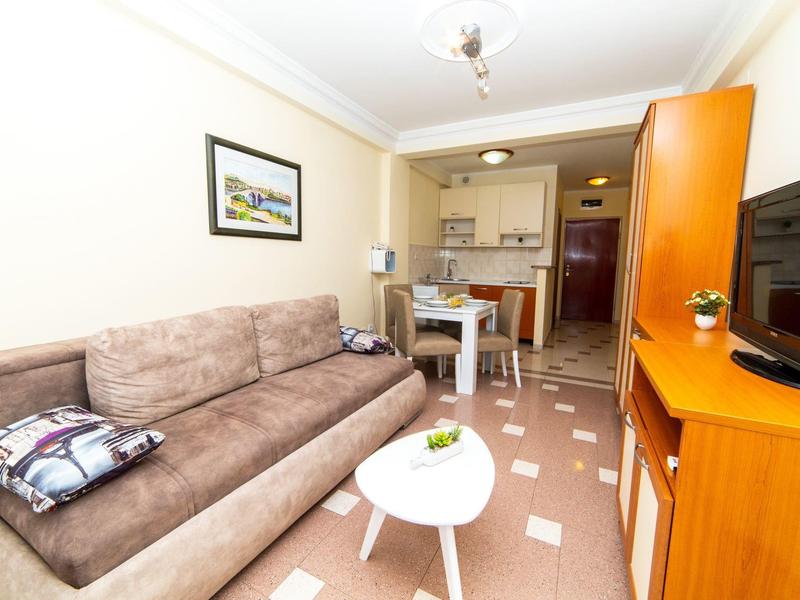 Helles Wohnzimmer mit braunem Sofa, kleinem weißen Tisch, Esstisch und orangefarbenem TV-Schrank.