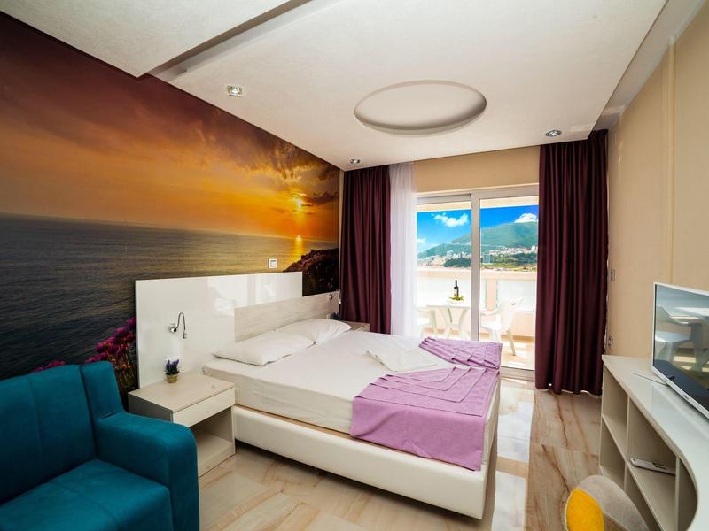 Modernes Hotelzimmer mit Doppelbett, Meerblick, Fernseher und gemütlichem blauen Sessel.