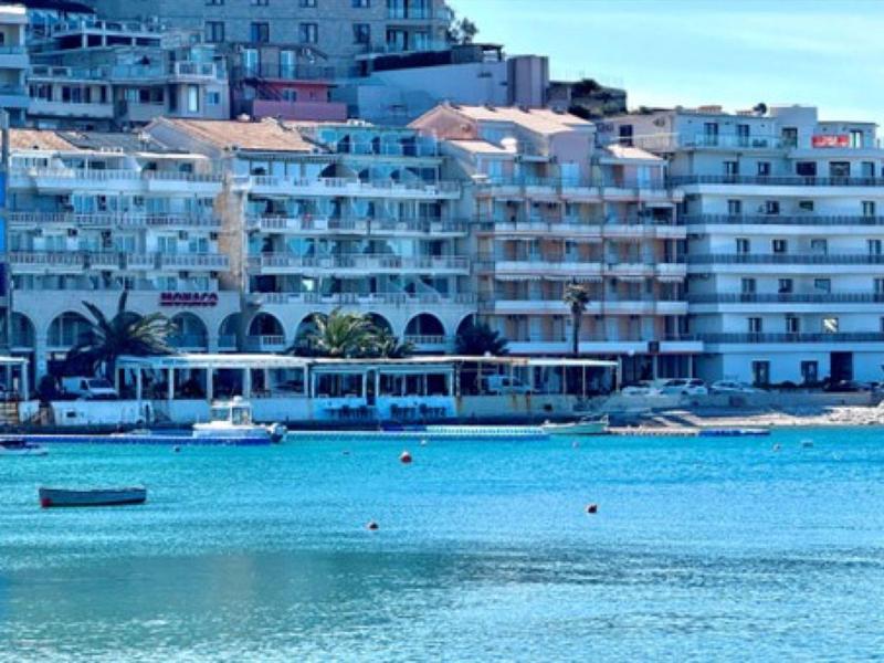 Blick auf Hotelanlage mit Balkonen am klaren blauen Wasser und mehreren kleinen Booten.