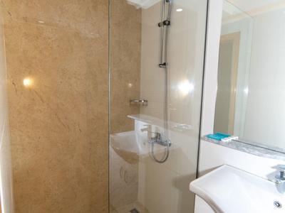 Kleines Badezimmer mit Glasdusche, weißem Waschbecken und Spiegel, beige Fliesen an Wand und Boden.