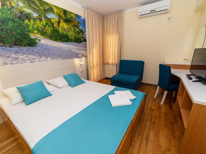 Modernes Schlafzimmer mit Doppelbett, blauer Bettdecke, Schreibtisch und großem Wandbild vom Strand.