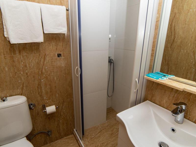 Kleines Badezimmer mit Eckdusche, weißem WC, Waschbecken und Holzoptikfliesen an Wand und Boden.