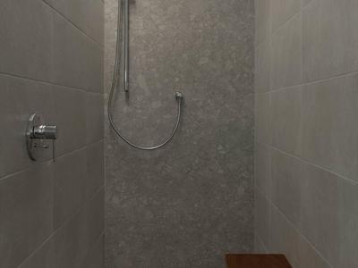 Moderne begehbare Dusche mit Regenduschkopf und Holzbank in neutralen Grautönen.