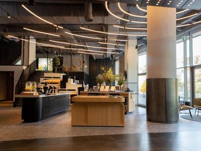 Modernes Hotelfoyer mit Empfangstresen, Sitzbereich und großen Fenstern für viel Tageslicht.