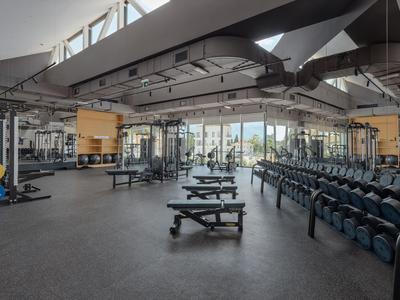 Heldere fitnessruimte met gewichten, banken en grote ramen in een hotel.