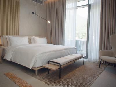 Helles Hotelzimmer mit großem Bett, gemütlichem Sessel und Zugang zu einem Balkon.