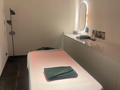 Schlicht eingerichteter Massageraum mit beleuchtetem Spiegel und Handtüchern auf der Liege.