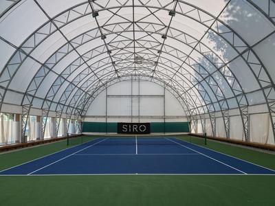 Overdekte tennisbaan met blauw speelveld en groene randen in een hal van witte stof