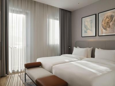 Modernes Hotelzimmer mit zwei Einzelbetten, großen Fenstern und weichen Vorhängen.