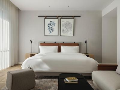 Modernes, helles Schlafzimmer mit großem Bett, Kunst an der Wand und gemütlichen Sitzgelegenheiten.