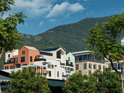 Modernes Hotelgebäude vor bewaldetem Berg unter blauem Himmel mit Wolken.