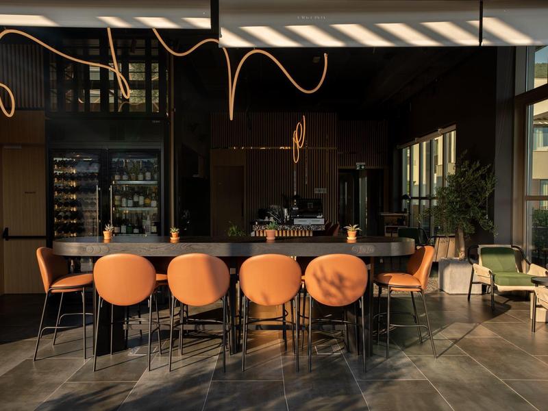 Moderner Hotelbarbereich mit runden orangen Barhockern und indirekter Beleuchtung.