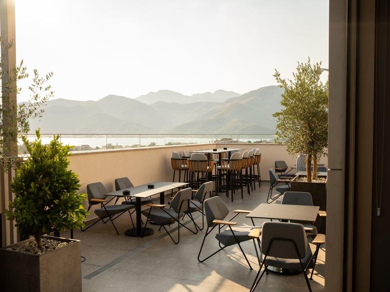 Terrasse mit Stühlen und Tischen, Blick auf Berglandschaft und See bei Sonnenuntergang.