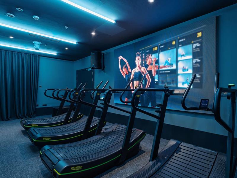 Modernes Fitnessstudio mit Laufbändern und großem Bildschirm im Hintergrund.