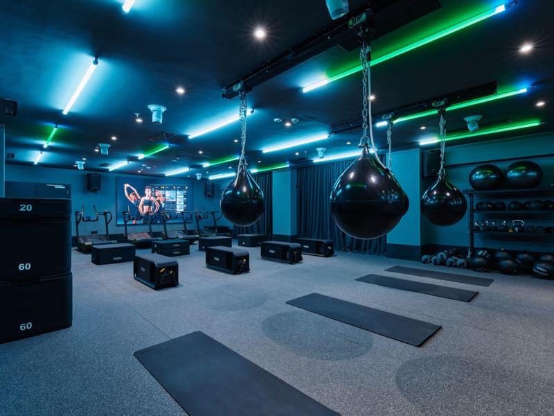 Dunkler Fitnessraum mit Neonbeleuchtung, Schlagsäcken und Yogamatten auf dem Boden.