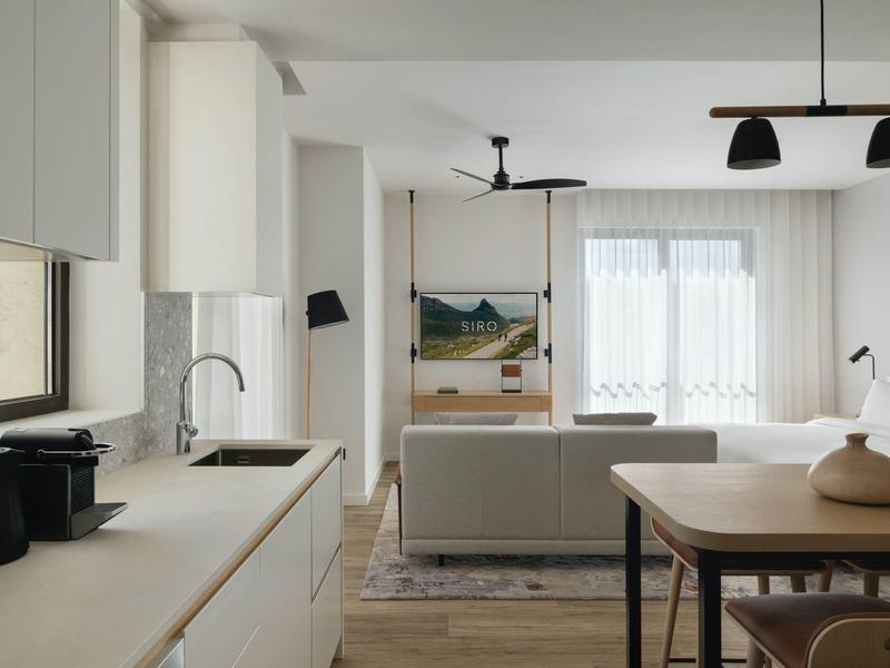 Helles, modernes Wohnzimmer mit offener Küche, Esstisch und großer Fensterfront.