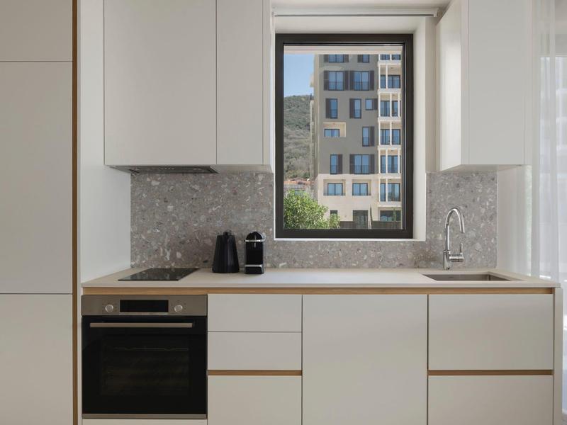 Moderne weiße Küchenzeile mit großem Fenster und Blick auf ein urbane Gebäude.