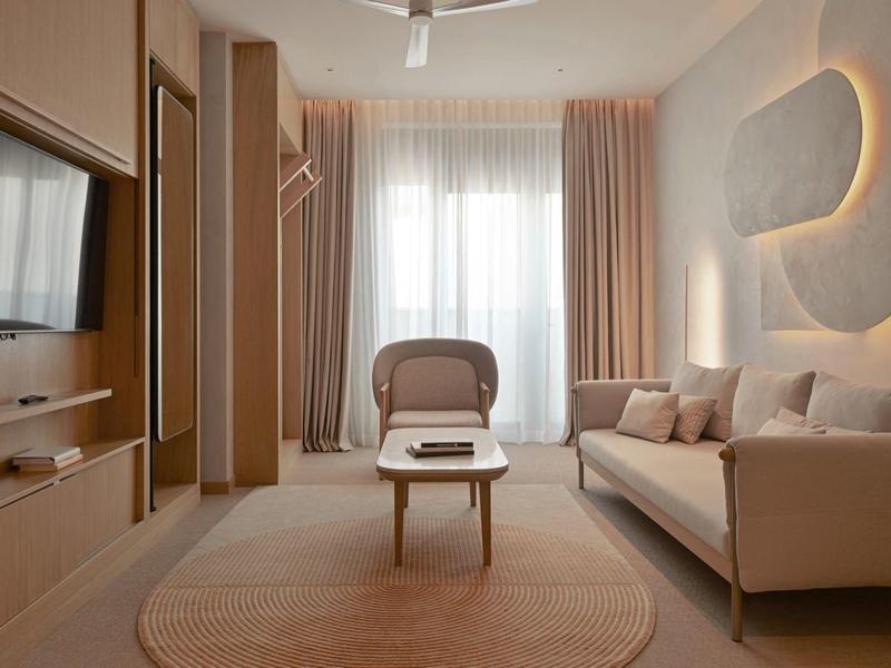 Modern eingerichtetes Wohnzimmer mit Sofa, Sessel, großem Fenster und warmem Holzdesign.