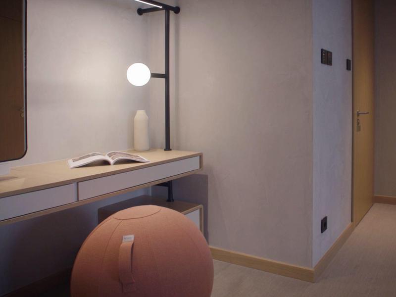 Moderner Hotel-Schreibtisch mit runder Hocker, Buch und runder Leuchte an der Wand.