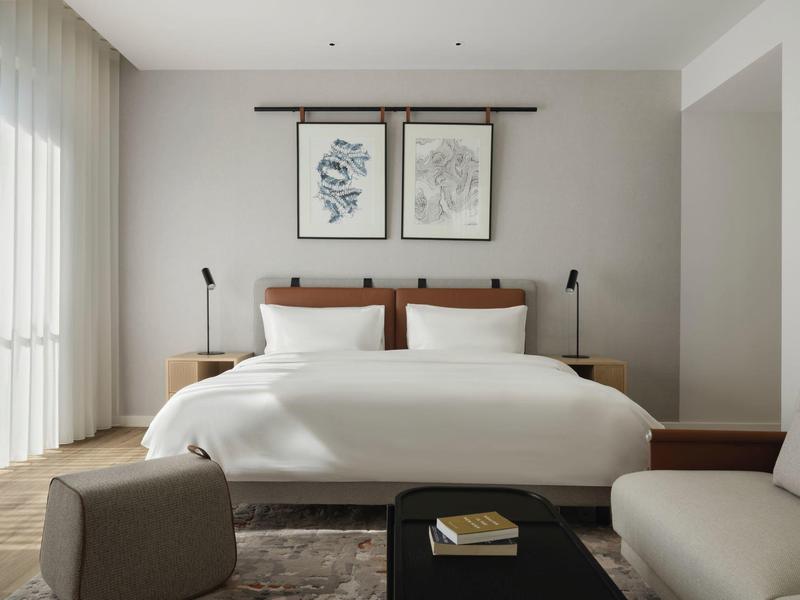 Modernes, helles Schlafzimmer mit großem Bett, Kunst an der Wand und gemütlichen Sitzgelegenheiten.