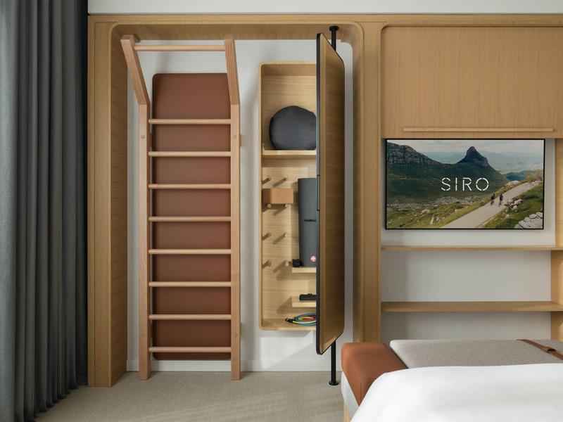 Modernes Hotelzimmer mit Holztreppe, Spiegel, Fernseher und Bett mit weißen Laken.