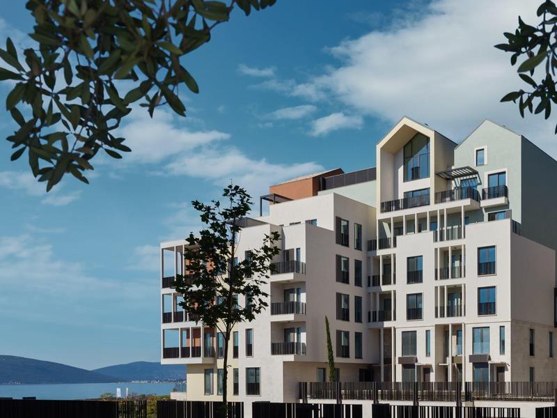 Moderner mehrstöckiger Wohnkomplex mit Balkonen unter blauem Himmel und Bäumen.