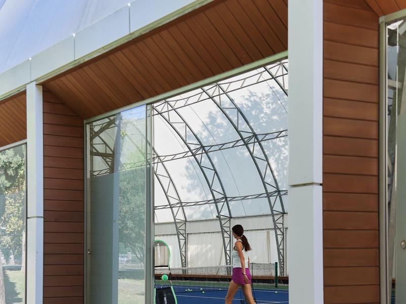 Außenansicht eines modernen Gebäudes mit Glasfassade und einem Tennisplatz im Inneren.