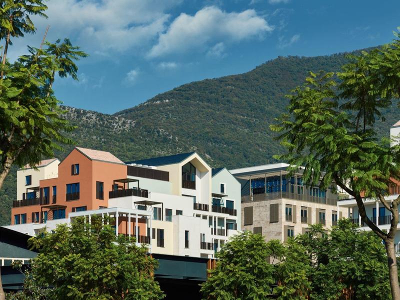 Modernes Hotelgebäude vor bewaldetem Berg unter blauem Himmel mit Wolken.