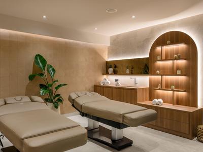 Salle de spa minimaliste avec deux tables de massage, éclairage encastré et accents de plantes.