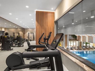 Salle de sport moderne avec équipements et vue sur la piscine de l'hôtel.
