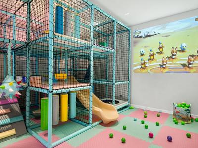 Espace de jeux pour enfants à l'hôtel avec structure d'escalade, toboggan et tapis colorés.