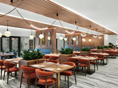 Restaurant moderne avec tables en bois, chaises rouges et éclairage suspendu dans un hôtel.