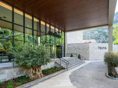 Entrée d'hôtel moderne avec façade en verre, plafond en bois et plantes à l'extérieur.