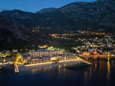 Hôtel éclairé au bord de l'eau avec des montagnes en arrière-plan la nuit.
