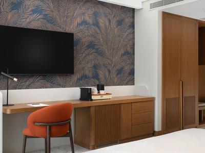 Modernes Hotelzimmer mit Schreibtisch, Stuhl und Fernseher an gemusterter Wand.