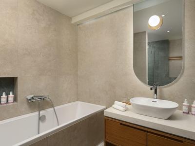 Modernes Badezimmer mit Badewanne, ovalem Spiegel und Waschtisch mit Holzschrank.