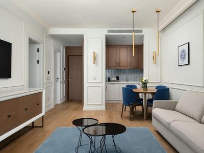 Modern eingerichtetes Wohnzimmer mit Sofa, blauer Teppichmatte und integriertem Küchenbereich in einem Hotelzimmer.